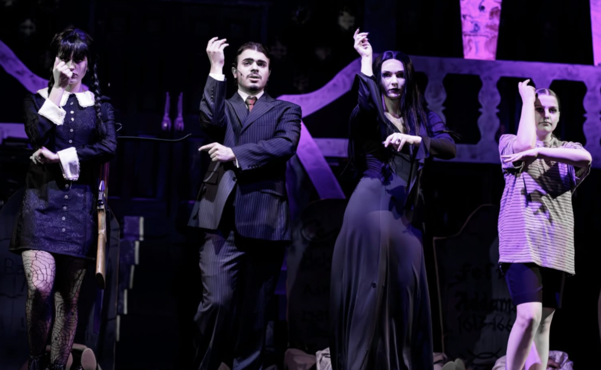 Wednesday, Gomez, Morticia, and Pugsley Addams stand snapping 